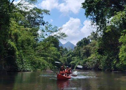 Two girls sit in a kayak on a river, holding their paddles above their heads