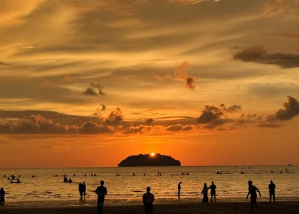 People on a beach silhouetted by an orange sunset