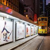 Yellow tram travelling along tracks alongside advertisements at night