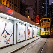 Yellow tram travelling along tracks alongside advertisements at night