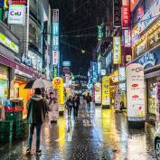 Image of a Korean city in the rain at night, with neon signs and people walkign