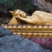 Reclining gold gilt buddha on purple platform surrounded by craggy rocks