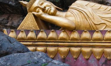 Reclining gold gilt buddha on purple platform surrounded by craggy rocks