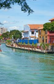 Boats with people navigate river traversing Malacca city in Malaysia