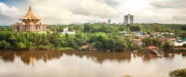 Aerial view of Kuching, with the new parliament house and other buildings strewn along the river and lined with jungle. 