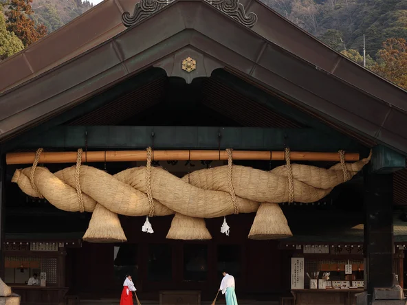 Two ladies in traditional dress sweeping front of wooden shrine