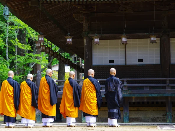 Monks in orange robes lined up to pray outside wooden temple 