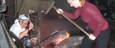 Lady assisting Japanese swordsmith banging metal 
