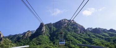 Cable car going up rocky mountains covered in tress in Seoraksan, South Korea