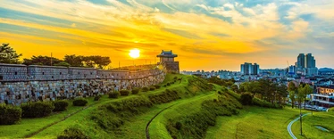 Suwon fortress walls at sunset with city skyline in background