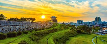 Suwon fortress walls at sunset with city skyline in background