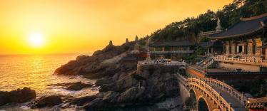 Sun setting over sea next to ornate temple and bridge in Busan 