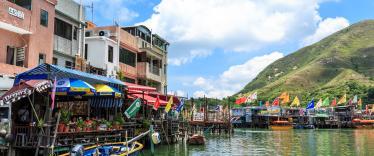 Fishing boats docked up by covered jetties alongside colourful houses 