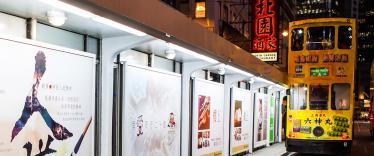 Yellow tram travelling along tracks alongside advertisements at night 