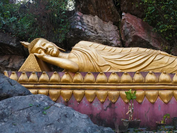 Reclining gold gilt buddha on purple platform surrounded by craggy rocks