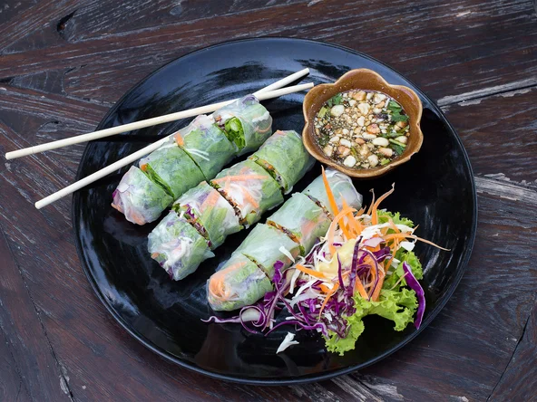 Delicious Vietnamese rice paper spring rolls sit in a dish on a wooden table