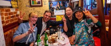 A group of people posing with peace signs at a table filled with food and drinks