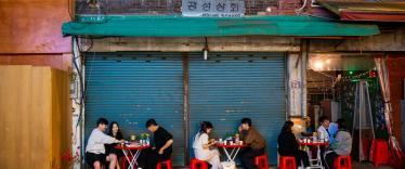 Local South Koreans enjoying food whilst sitting outside on red stools in a street restaurant