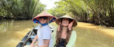 Two female travellers on a boat in Vietnam wearing traditional hats