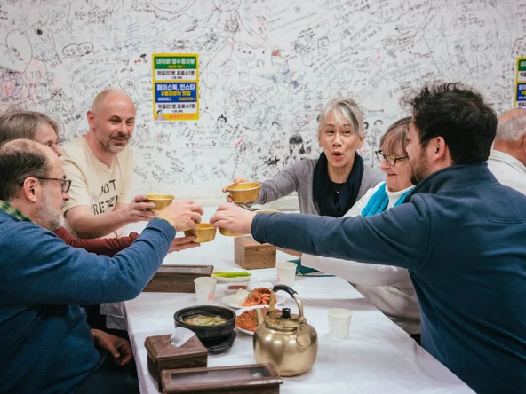 Group enjoying traditional Korean meal with brass bowls and teapot in a vibrant restaurant covered in handwritten notes