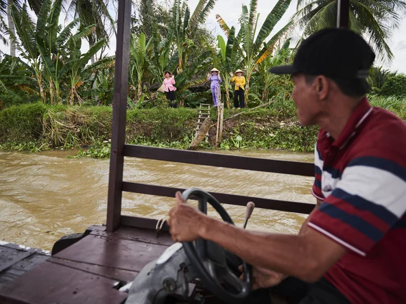 A local Vietnamese boat driver on the Mekong Delta being waved to by women in the jungle on a boat cruise