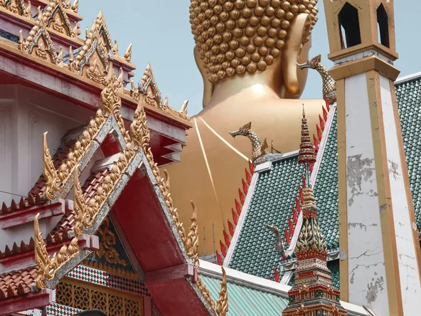 Giant golden buddha statue between traditional thai rooftops in Bangkok, Thailand