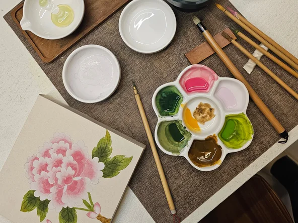 Korean traditional painting of a peony flower and some paints and paint brushes