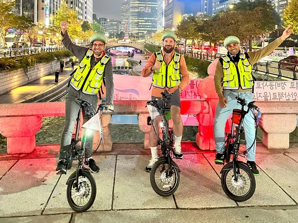 3 men on e-bikes posing in front of Cheonggyecheon stream