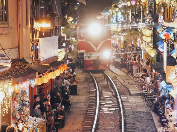 A train approaches along the tracks, with shops and lights tightly packed on either side