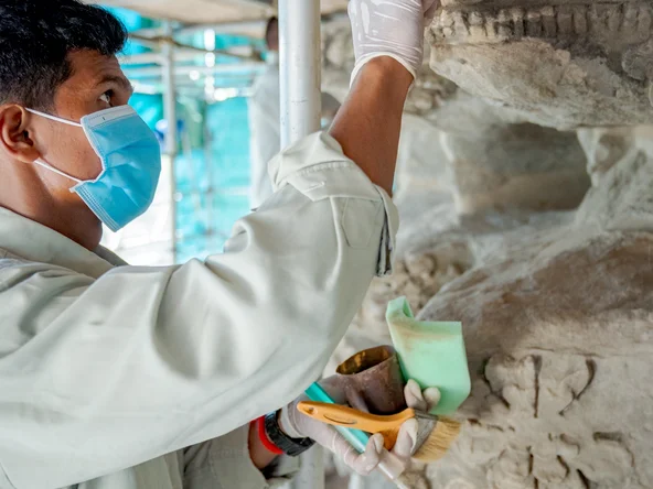 A conservation expert uses a small brush to repair a wall in the Angkor Wat temple complex
