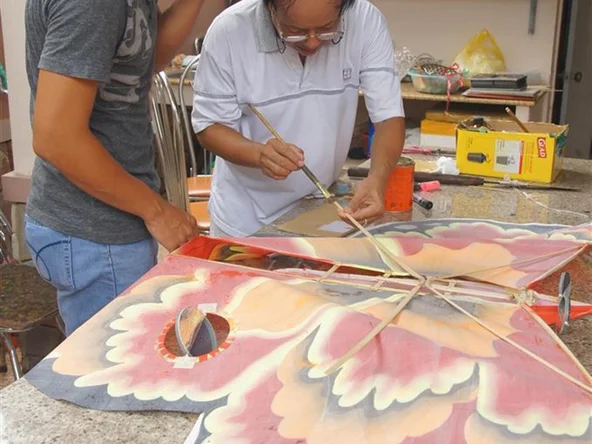 A man makes a kite of an orange and yellow butterfly out of silk and bamboo