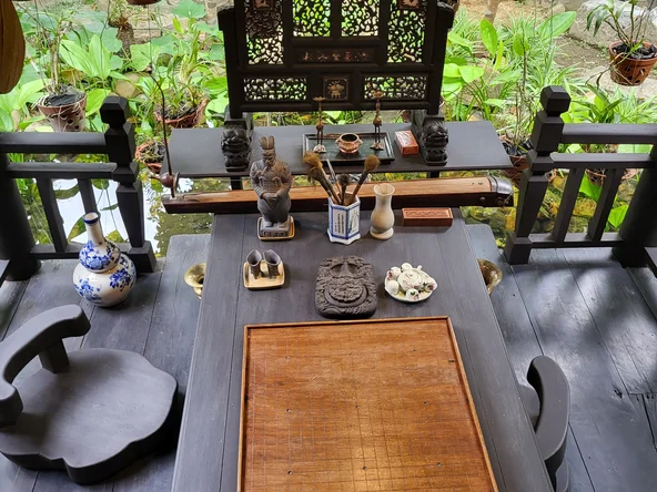 A selection of artefacts sit on a wooden table low to the floor. In the background, a collection of green plants