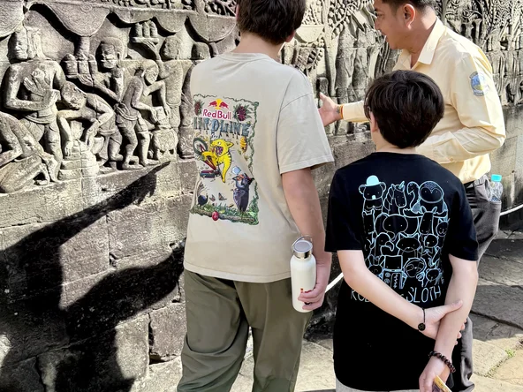Two teenaged boys look at the murals on a temple wall with their guide