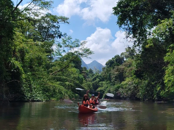 Two girls sit in a kayak on a river, holding their paddles above their heads