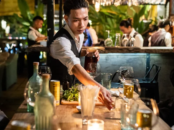 A bartender lines up cocktail ingredients on a wooden table for a hands-on lesson