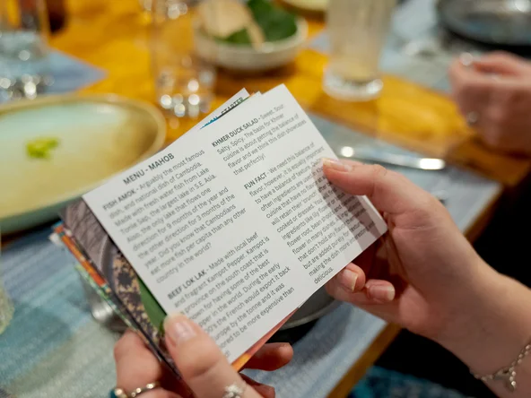 A pair of hands holding a card over a table, listing details of the food available