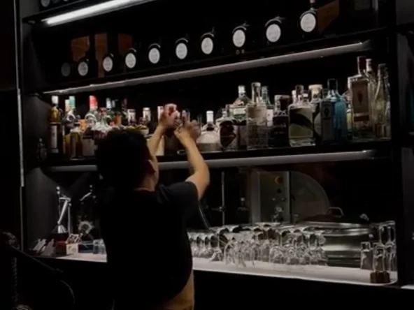 A bartender selects a bottle from a wall filled with different spirits
