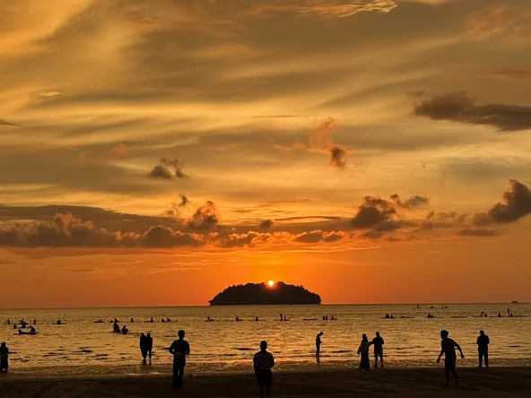 People on a beach silhouetted by an orange sunset