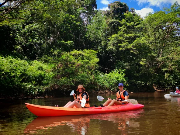 Two girls sit in a kayak paddling down a river in the rainforest