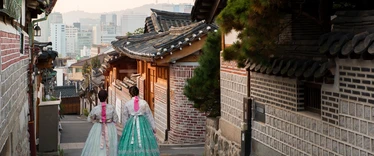 Back of two women wearing hanbok walking through the traditional style houses of Bukchon Hanok Village in Seoul, South Korea.