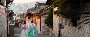 Back of two women wearing hanbok walking through the traditional style houses of Bukchon Hanok Village in Seoul, South Korea.