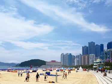 People walking along sandy beach with skyscrapers of Busan in background