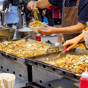 Street food vendor spooning vegetable noodles into takeaway bowl 