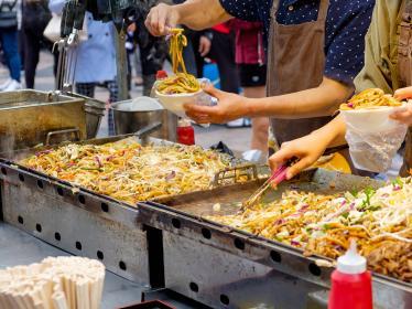 Street food vendor spooning vegetable noodles into takeaway bowl