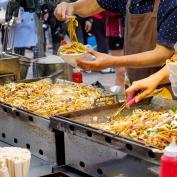 Street food vendor spooning vegetable noodles into takeaway bowl 