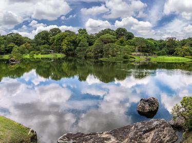 Beautiful blue sky and clouds reflected on a pond in Rikugien garden, surrounded by beautiful greenery