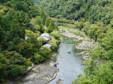 Boats gently navigating on Hozugawa river surrounded by forested mountains in Arashiyama, Kyoto