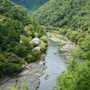 Boats gently navigating on Hozugawa river surrounded by forested mountains in Arashiyama, Kyoto