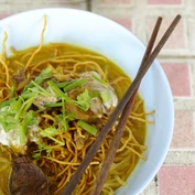 Bowl of curry noodles with chopsticks and lime to garnish 