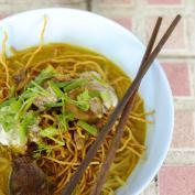 Bowl of curry noodles with chopsticks and lime to garnish 